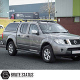 Silver-grey Nissan Navara with Truckman Grand Hardtop Canopy featuring remote locking, tinted pop-out windows, and a sleek cab-high design, parked in front of an industrial building.
