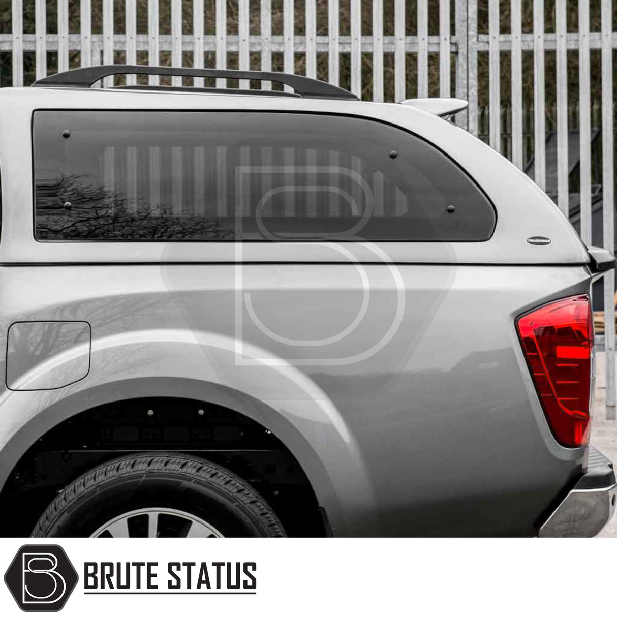Silver Nissan Navara with Truckman Grand Hardtop Canopy, featuring tinted windows, roof rails, and rear quarter view, highlighting aftermarket design and remote locking.