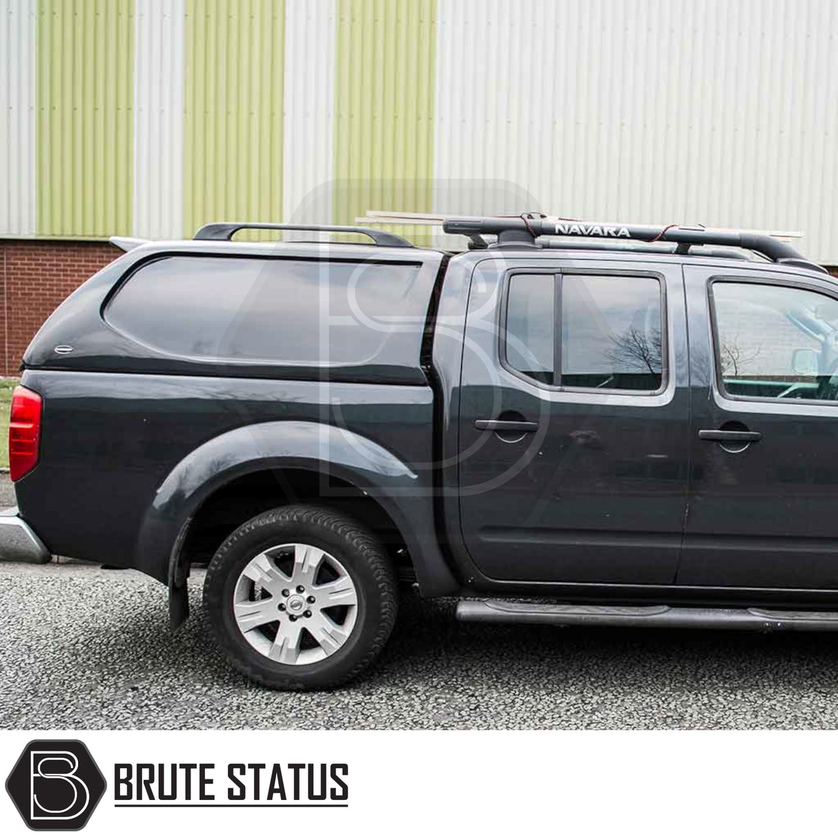 Nissan Navara 2005-2015 D40 with Truckman L-Series Hardtop Canopy featuring remote locking, matching canopy, roof rack, and alloy wheels, parked in front of a building.