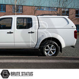 Side view of Nissan Navara 2005-2015 D40 with Truckman L-Series Hardtop Canopy featuring remote locking, parked by an industrial building.