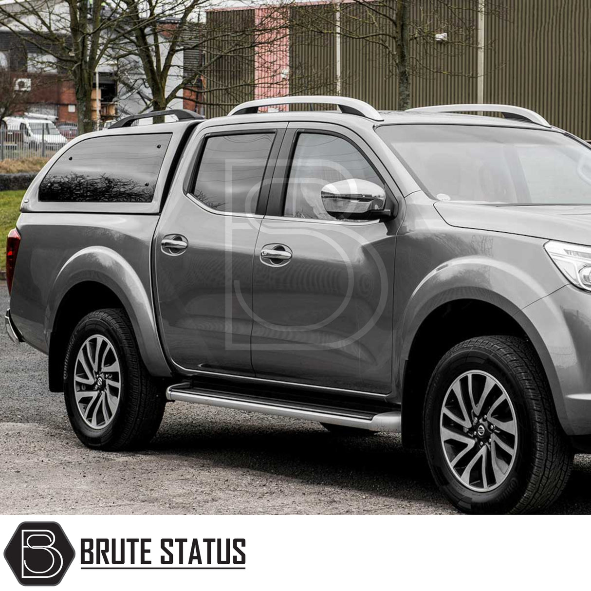 Nissan Navara with Truckman Grand Hardtop Canopy, featuring remote locking, roof rails, and tinted pop-out side windows, parked on gravel by industrial buildings.