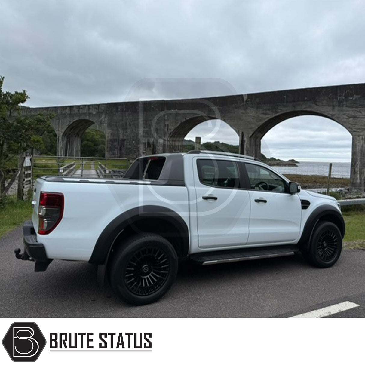White pickup truck with Obsidian OB2 Gloss Black wheels parked by a stone viaduct, showcasing Brute Status's aftermarket customization expertise.