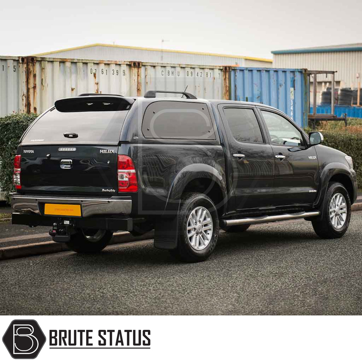Toyota Hilux 2005-2016 Truckman Grand Hardtop Canopy with remote locking, displayed on a black pickup truck with a color-matched canopy in an industrial setting.
