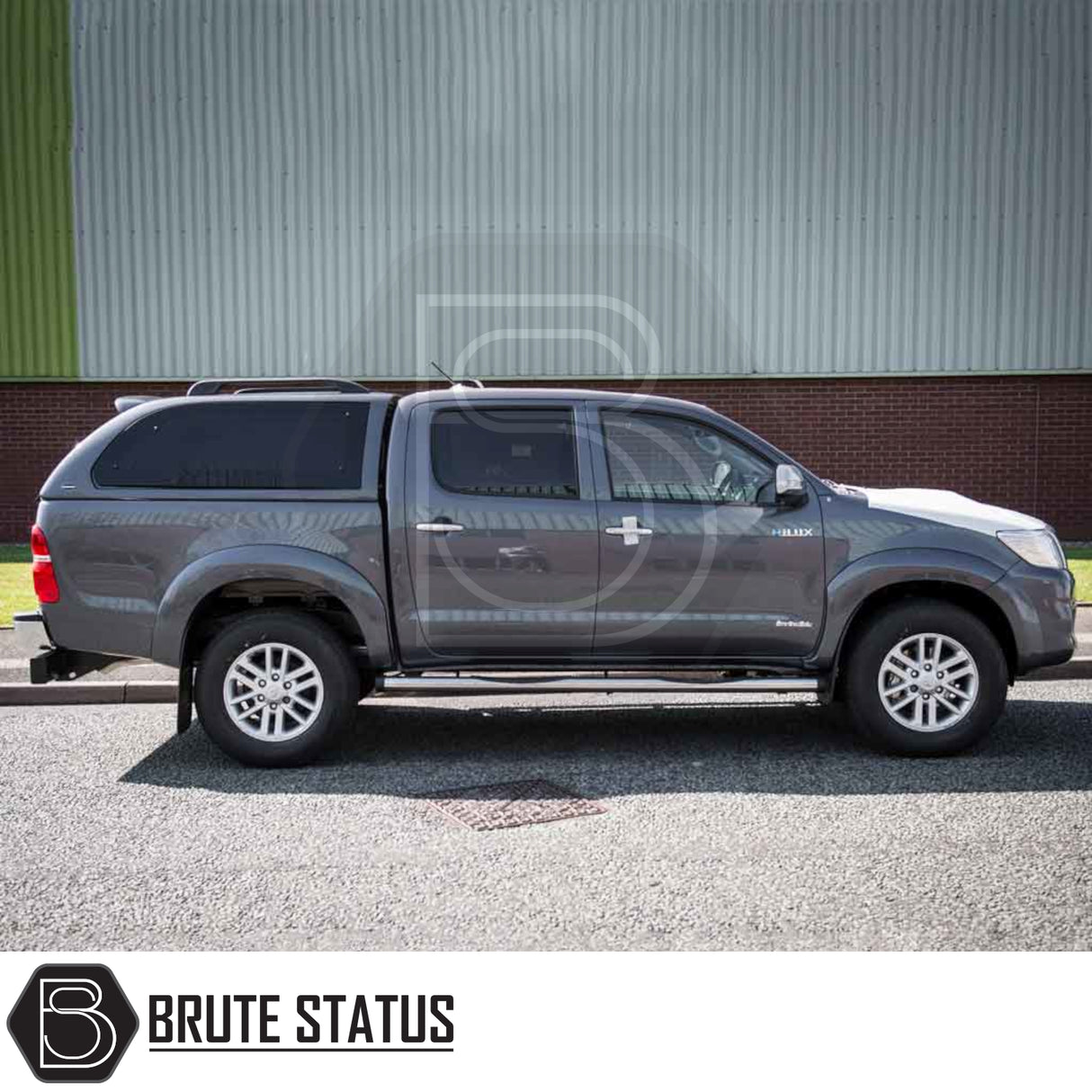 Toyota Hilux 2005-2016 with Truckman Grand Hardtop Canopy featuring remote locking, pop-out tinted windows, parked in front of a corrugated-metal building.