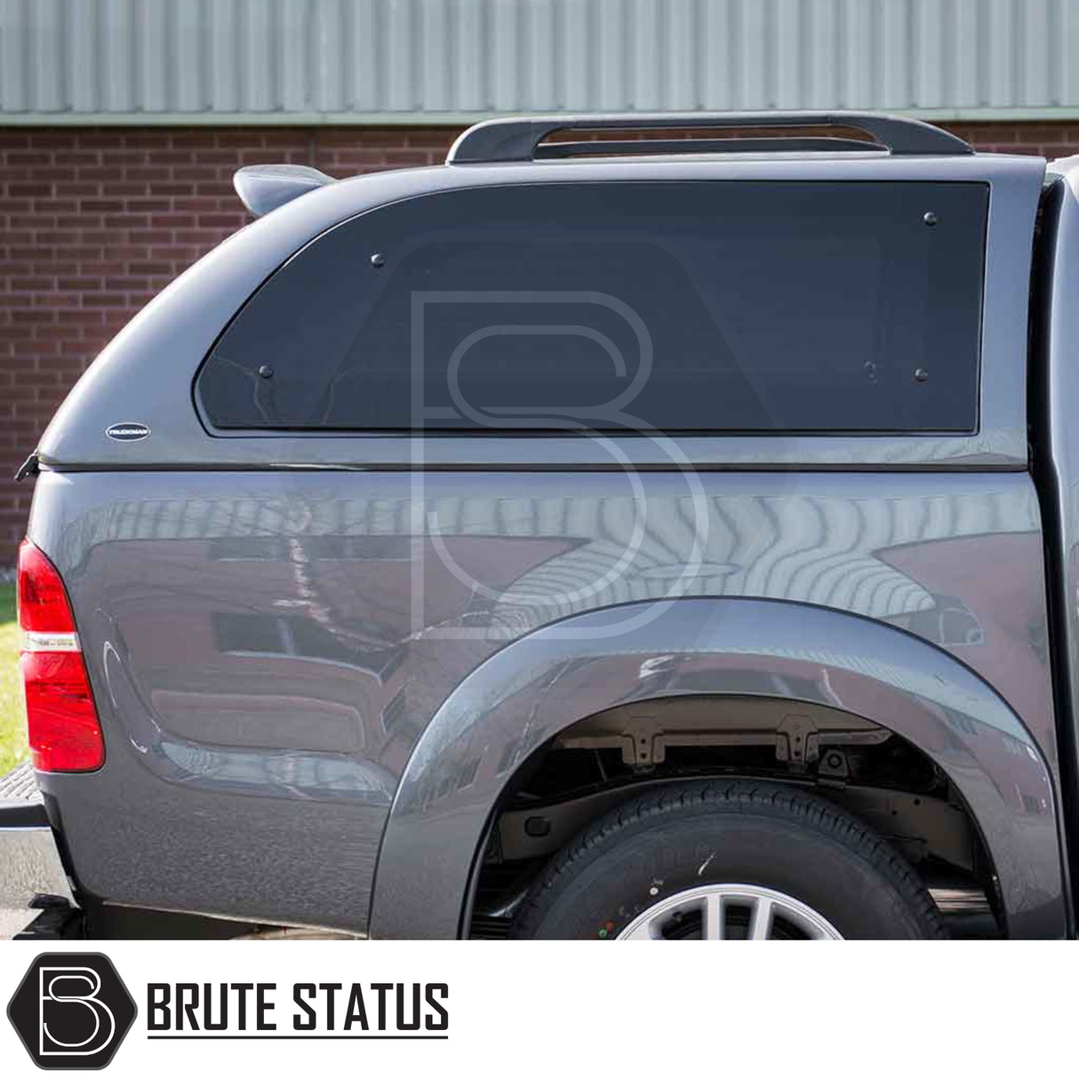 Rear-quarter view of a gray Toyota Hilux 2005-2016 with a Truckman Grand Hardtop Canopy, featuring tinted side windows and a roof rack.