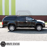 Toyota Hilux 2005-2016 MK6, MK7 Truckman Grand Hardtop Canopy with remote locking, cab-high design, and tinted pop-out windows beside corrugated-metal building.