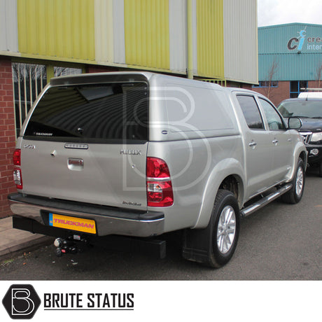 Toyota Hilux 2005-2016 MK6, MK7 Truckman RS Hardtop Canopy with glazed rear window, solid sides, parked outside an industrial building, showcasing tow hitch and alloy wheels.