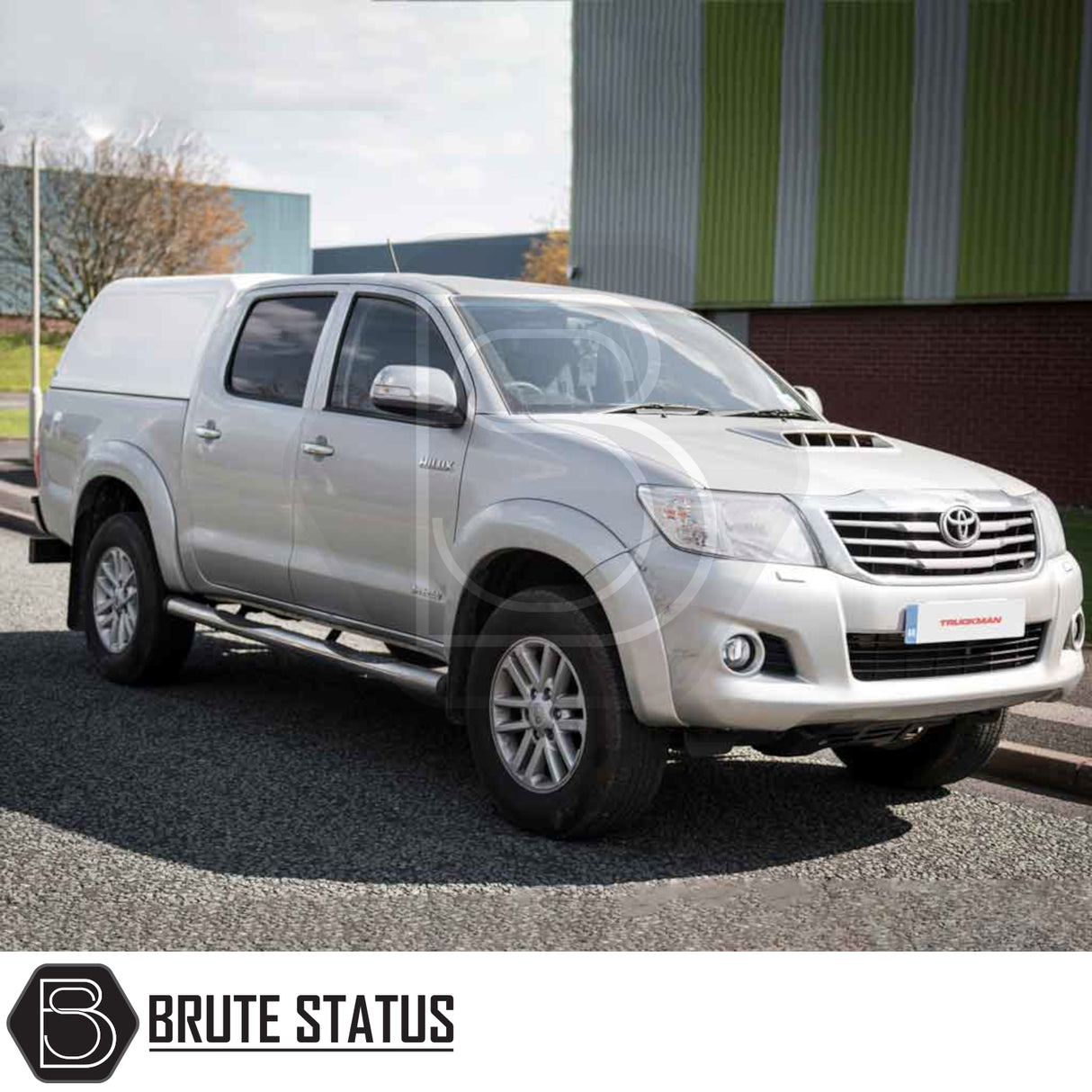 Silver Toyota Hilux with Truckman RS Hardtop Canopy featuring glazed rear window, parked in front of an industrial building.
