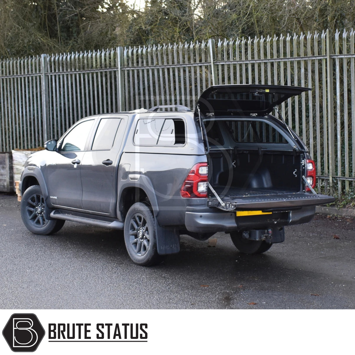 Toyota Hilux Invincible X with Truckman GLS hardtop canopy, featuring remote locking and sliding windows, displayed open beside a security fence, highlighting enhanced storage and security.