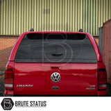 Rear view of a red Volkswagen Amarok fitted with a Truckman GLS Hardtop Canopy, featuring lockable sliding windows and a concealed lock handle, parked near a metal wall.